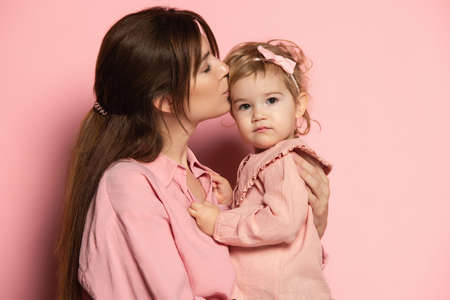 Kiss. Portrait of young woman and little girl, mother and daughter isolated on pink studio background. Mothers Day celebration. Concept of family, childhood, motherhoodの写真素材