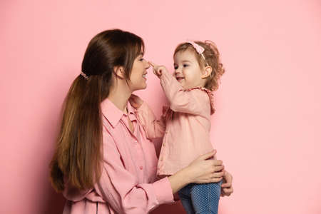Happy woman and little girl, caring mother and daughter isolated on pink studio background. Mothers Day celebration. Concept of family, childhood, motherhoodの写真素材