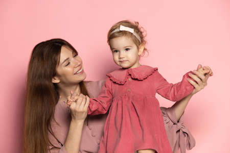 Delighted young woman and toddler, caring mother and daughter isolated on pink studio background. Mothers Day celebration. Concept of family, childhood, motherhoodの写真素材