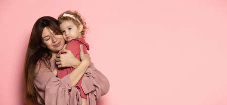 Hugs. Delighted young woman and toddler, caring mother and daughter isolated on pink studio background. Mothers Day celebration. Concept of family, childhood, motherhoodの写真素材