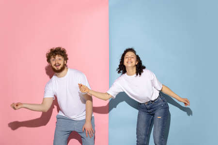 Emotional couple of young funny and happy man and girl dancing hip-hop at studio on blue and pink...