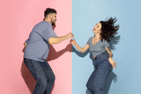 Young excited couple of funny and happy man and girl dancing hip-hop, having fun isolated on blue...