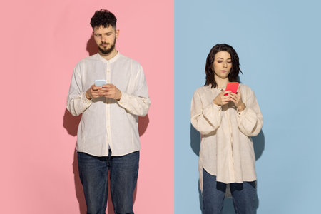 Studio shot of young emotive man and girl using phones isolated on blue and pink trendy color...