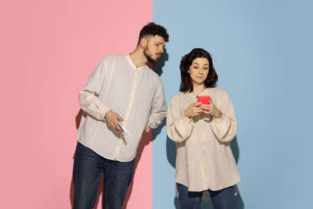 Studio shot of young emotive man and girl using phones isolated on blue and pink trendy color background. Human emotions, care, relationships conceptの写真素材