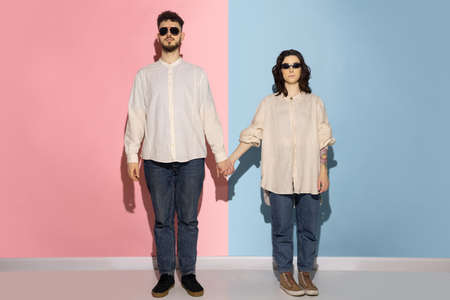 Young serious man and girl wearing casual denim clothes standing isolated on blue and pink trendy color background. Emotions conceptの写真素材