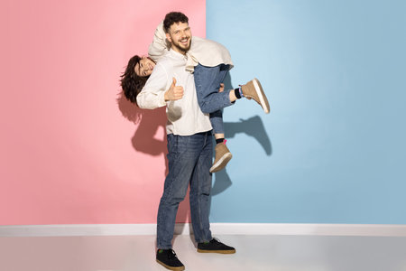Emotional couple of young funny and happy man and girl having fun studio on blue and pink trendy...