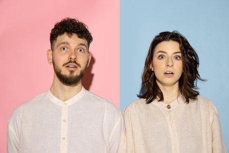 Half length portrait of young emotive man and girl looking at camera isolated on blue and pink...