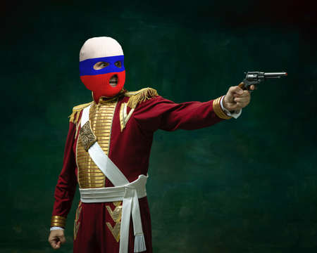 Portrait of man in suit as Nicholas II wearing red, white and blue balaclava isolated on dark green background. Retro style, comparison of eras concept. Historyの写真素材