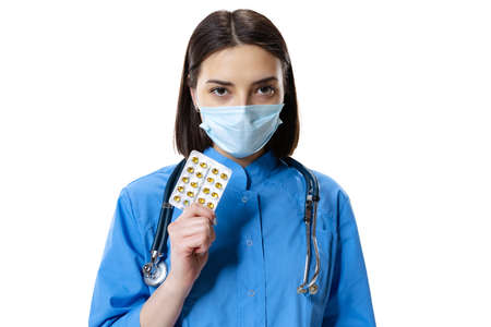 Portrait of young woman, doctor, therapeutic or medical advisor wearing face mask and blue uniform isolated on white background.の写真素材