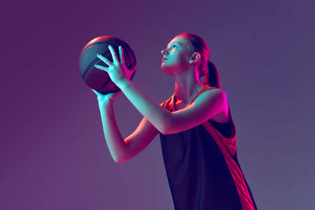 Portrait of sportive girl, basketball player training, preparing to throw a ball isolated over gradient pink purple background in neonの写真素材