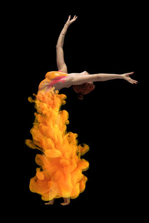 Full-length portrait of young emotive woman covered with orange dye splash dancing, posing isolated over black backgroundの写真素材