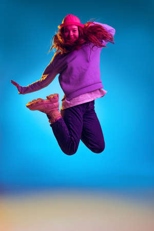 Portrait of young stylish girl posing in a jump isolated over blue studio background in pink neon lightの写真素材