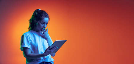 Half-length portrait of young girl reading shocking news on tablet isolated over gradient red...