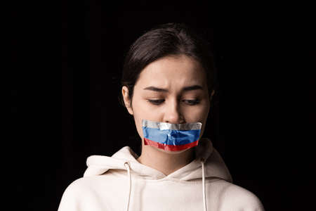 Half-legth portrait of young emotional upset girl with three colors duct tape over her mouth...