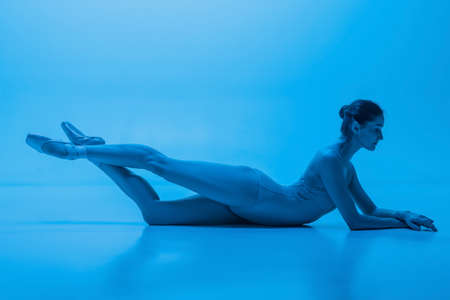 Portrait of beautiful graceful ballet dancer posing isolated on blue studio background in neon light. Art, motion, action, flexibility concept.の写真素材