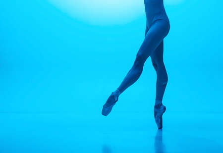 Close-up ballerinas legs in pointe shoes isolated on navy color studio background in neon. Art, motion, action, flexibility, inspiration concept.の写真素材