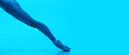 Close-up ballerinas legs in pointe shoes isolated on navy color studio background in neon. Art, motion, action, flexibility, inspiration concept.の写真素材