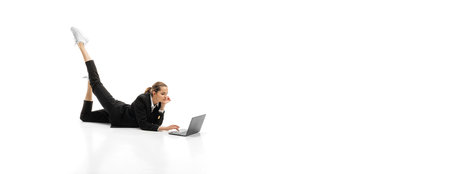 Portrit of young businesswoman in official black suit lying on floor and typing on laptop isolated...