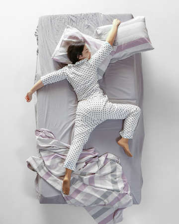 Aerial view young sleeping girl in white pajamas lying in big gray bed. Concept of health, home interior, relax time, family, dreamsの写真素材