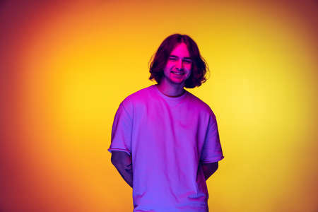 Portrait of young man, student in casual clothes isolated on orange background in purple neon light. Concept of emotions, beauty, fashionの写真素材