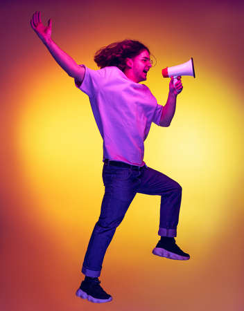 Full-length portrait of young excited man jumping with megaphone isolated on orange background in...