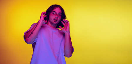 Studio shot of young scared man, student posing isolated on orange background in purple neon light....