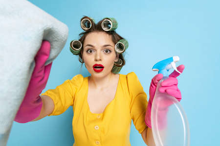 Shocked young pretty girl, housewife with curlers on her head isolated on blue studio background....