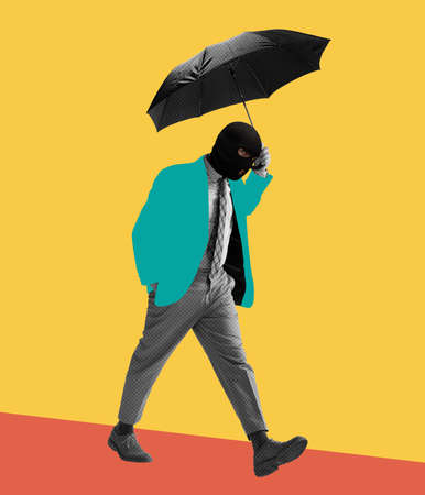 Contemporary art collage. Colorful design. Man in black balaclava walking with umbrella isolated over yellow backgroundの写真素材
