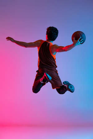 Young energetic man playing basketball isolated on gradient pink blue studio background in neon light. Youth, hobby, motion, activity, sport concepts.の写真素材