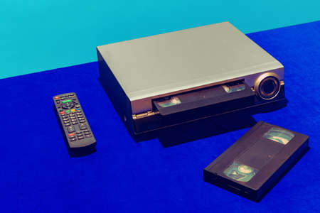 Pop art photography. Retro gadgets in modern life. Video recorder and cassette isolated on bright blue background. Vintage, retro fashion style. Concept of nostalgiaの写真素材
