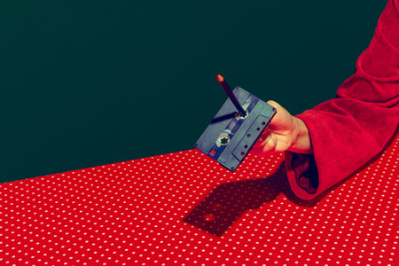 Female hand holding tape recorder cassette isolated on green and red background. Vintage, retro fashion style. Pop art photographyの写真素材