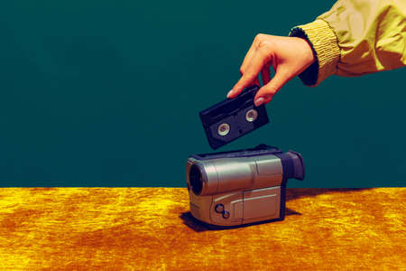 Concept of pop art photography. Using retro gadgets. Human hand holding videocamera isolated on green-yellow background. Vintage fashion style. Concept of nostalgiaの写真素材