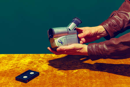 Concept of pop art photography. Using retro gadgets. Human hand holding videocamera isolated on green-yellow background. Vintage fashion style. Concept of nostalgiaの写真素材