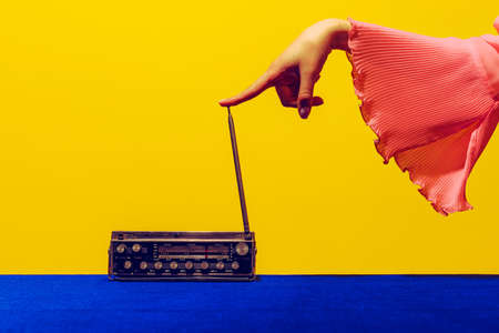 Old radio. Female hand touching radior, wireless isolated on bright blue and yellow background. Vintage, retro fashion style. Pop art photography.の写真素材