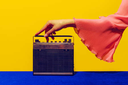 Old radio. Female hand touching radior, wireless isolated on bright blue and yellow background. Vintage, retro fashion style. Pop art photography.の写真素材