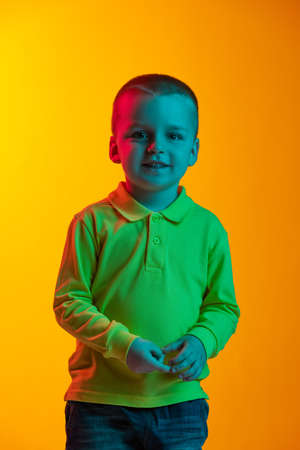 Portrait of cute little boy smiling isolated on yellow studio backgroud in neon light. Concept of child emotions, facial expression, childhoodの写真素材