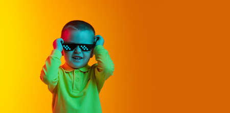Happy cute little boy, child smiling isolated on yellow studio backgroud in neon light. Concept of child emotions, facial expression, childhoodの写真素材