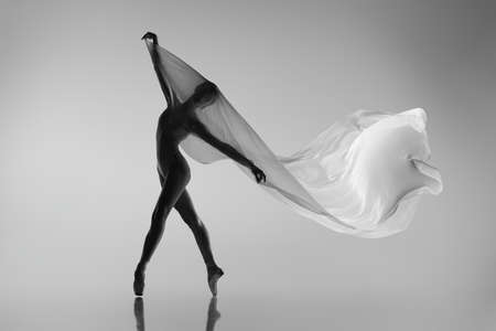 Black and white portrait of graceful ballerina dancing with fabric, cloth isolated on grey studio background. Grace, art, beauty concept. Weightless, flexible.の写真素材