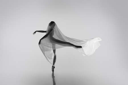 Black and white portrait of graceful ballerina dancing with fabric, cloth isolated on grey studio background. Grace, art, beauty concept. Weightless, flexible.の写真素材