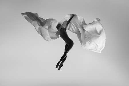 Black and white portrait of graceful ballerina dancing with fabric, cloth isolated on grey studio background. Grace, art, beauty concept. Weightless, flexible.の写真素材