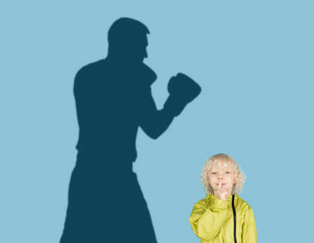 Conceptual image with boy and shadow of sportive male boxer, champion on blue background. Childhood, dreams, imagination, education concept.の写真素材