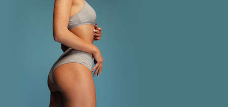 Cropped image of sportive female body, buttocks isolated over blue studio background. Model posing in gray cotton underwearの写真素材