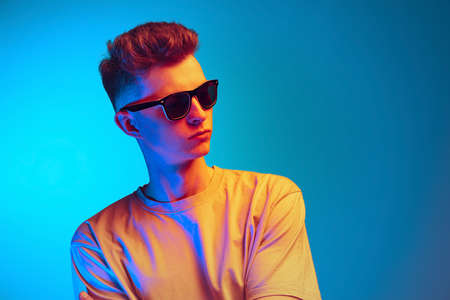 Studio shot of young emotional man, student in eyeglasses posing isolated over blue studio...