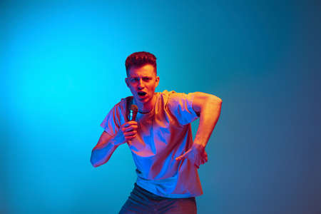 Musician, singer. Studio shot of young emotional man, student posing isolated over blue studio background. Action, sport, fashionの写真素材