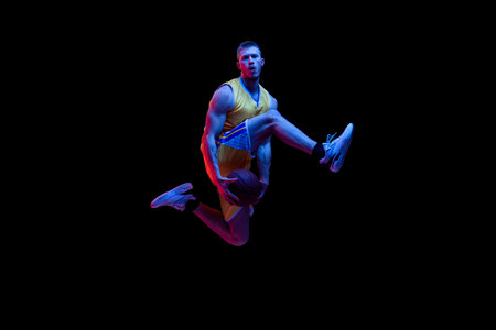 Portrait of sportive man, professional basketball player playing basketball isolated on dark background in neon light. Achievements, sport career, motion concepts.の写真素材