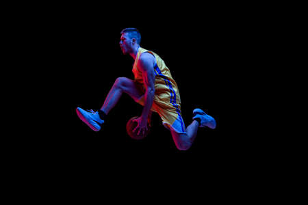 Portrait of sportive man, professional basketball player playing basketball isolated on dark background in neon light. Achievements, sport career, motion concepts.の写真素材