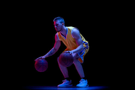 Dribbling. One sportive man, professional basketball player playing basketball isolated on dark...