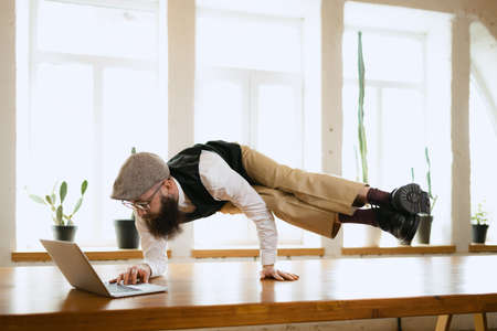 Emotional office clerk, young man doing yoga on wooden table in modern office at work time with...