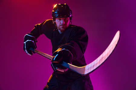 Professional male hockey player training in special uniform with helmet isolated over pink background in neon. Championの写真素材
