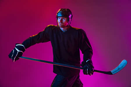 Man, professional hockey player training in special uniform with helmet isolated over pink background in neon. Defenderの写真素材